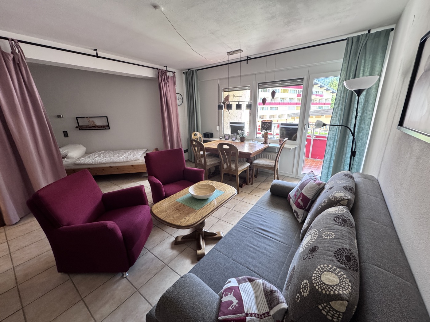 Heller Wohnraum mit Sofa, Sesseln, Esstisch und Zugang zum Balkon